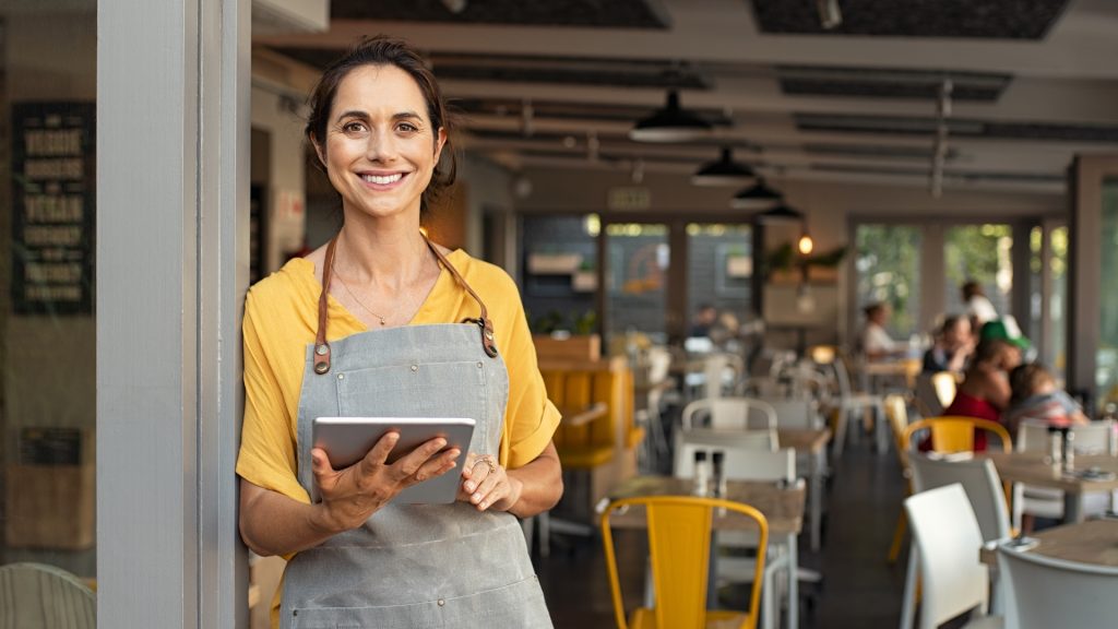 Mulher empreendedora sorridente utilizando tablet em seu restaurante.